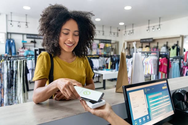 une femme qui paye avec son téléphone et une autre dame qui est derrière une caisse enregistreuse